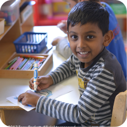 Child drawing and smiling in classroom.