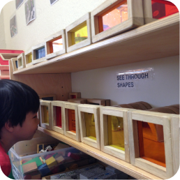 Child leaning toward translucent colored shape boxes