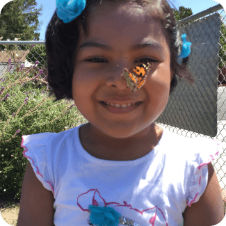 Child smiling with butterfly on her nose.