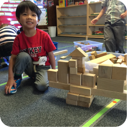 Child smiling next to wooden block structure.