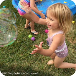 Child joyfully chasing a bubble outside.