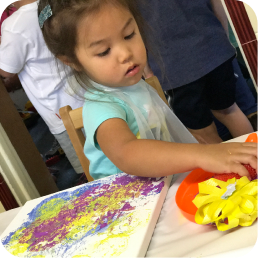Child painting with colorful tools and paper.