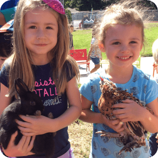 Two girls holding a rabbit and chicken.