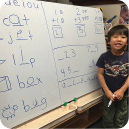 Child smiling next to whiteboard with writing.