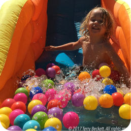 Child playing on water slide with balls.