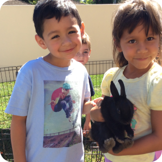 Children smiling, holding a black rabbit outside.