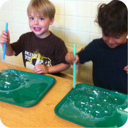 Two boys blowing bubble foam on green trays