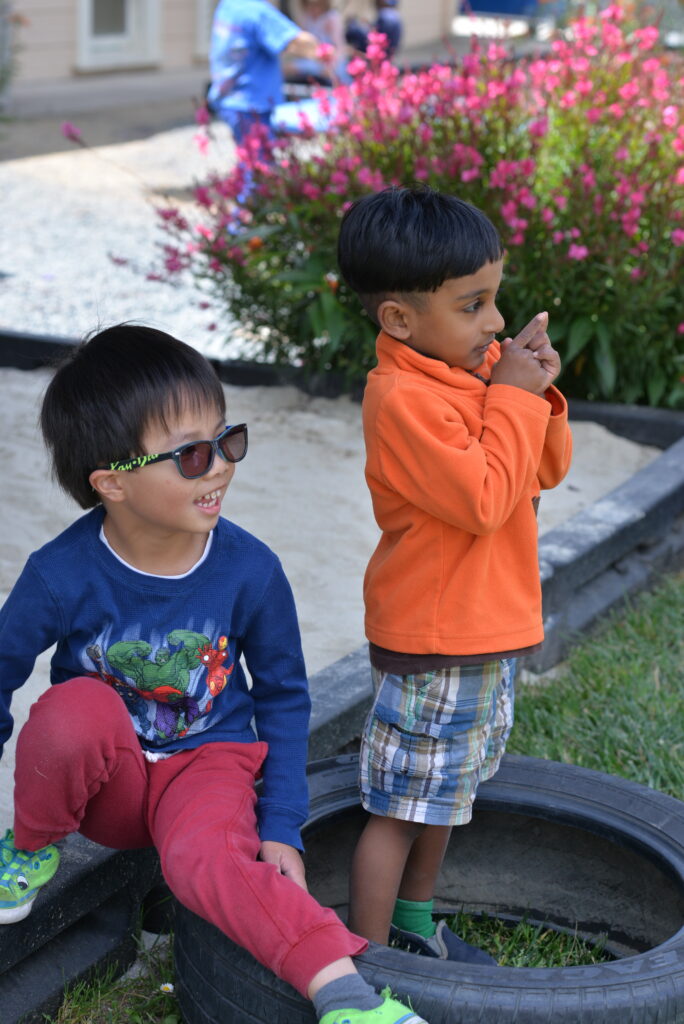 Two children playing near colorful flowerbed.