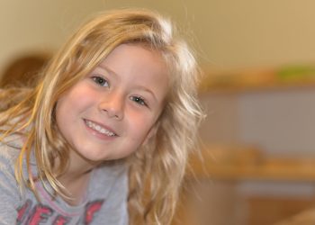 Smiling child with long blonde hair.