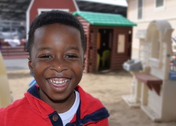 Smiling child at playground with playhouse.