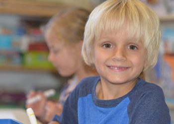 Smiling child in classroom with classmate.