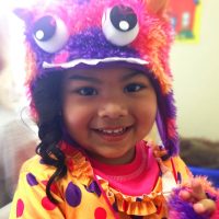 Child wearing colorful monster costume, smiling.
