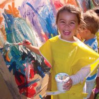 Child joyfully painting colorful mural outdoors.