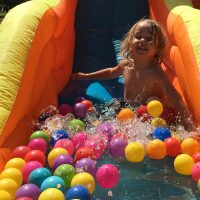 Child on water slide with colorful balls.