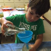 Child pouring liquid into a bottle funnel.