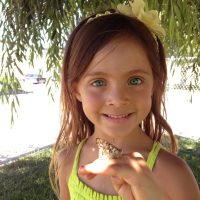 Girl smiling, holding butterfly on finger.
